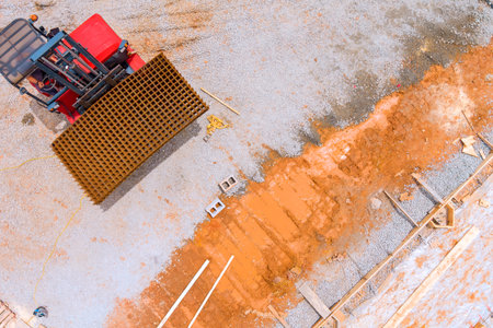 Heavy machinery operates at construction site, moving metal mesh preparing foundation during works...