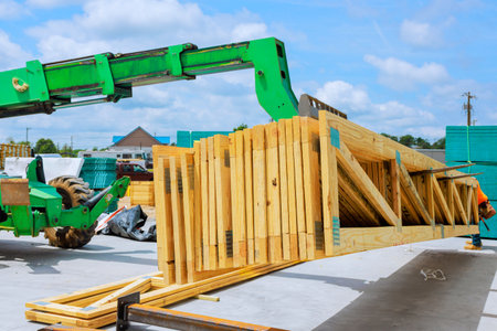 Construction worker uses green machine to lift wooden beams truss at site under works day time.