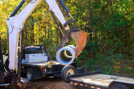 Heavy machinery is transporting drainage concrete pipe at construction site surrounded by forest