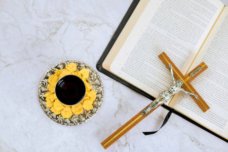 Table arranged for religious ceremony featuring bread, wine, crucifix, an open Bible on marble...