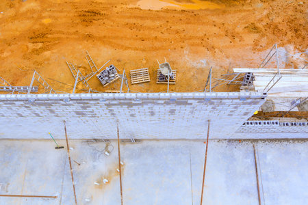 Workers are constructing wall with blocks, surrounded by building materials equipment at...