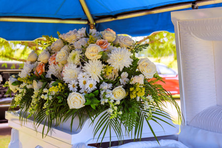 Beautiful display of white, pastel flowers adorns white casket at burial site under blue tent