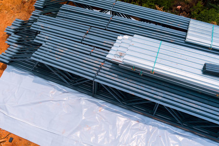 Steel beams are neatly arranged on construction site, with tarpaulins below for building preparation.の写真素材