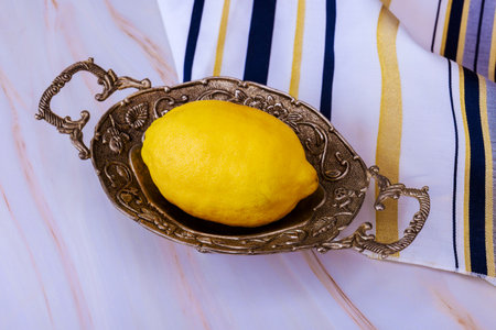 Traditional Jewish tallit prayer shawl on table during religious Sukkot festival, etrog fruit on...