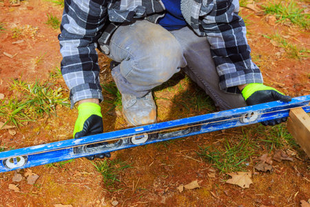 Worker checks leveling of wooden structure while kneeling on grass, ensuring precision in building...