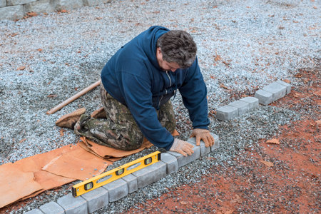 Worker carefully lays bricks for pathway, ensuring level placement on gravel surface during fall...