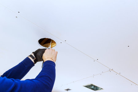Drywall is being modified as worker prepares to install new lighting fixtures in home renovation worksの写真素材