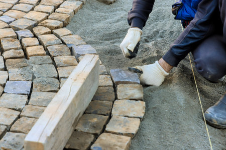 Laborer is placing cobblestones meticulously while constructing path at worksite during works day.の写真素材