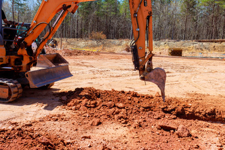 Excavator actively digs large trench of dirt at rural construction site.