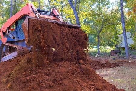 Heavy machinery removes soil in forested location, preparing land for future landscaping activities.