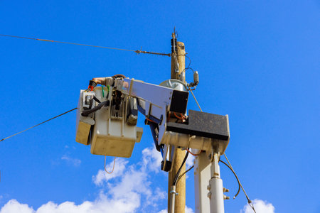 Maintenance crew uses bucket truck to check wires on tall utility pole under works dayの写真素材