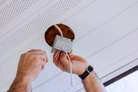 Electrical worker connects wires to junction box mounted in ceiling of renovated living space.の写真素材
