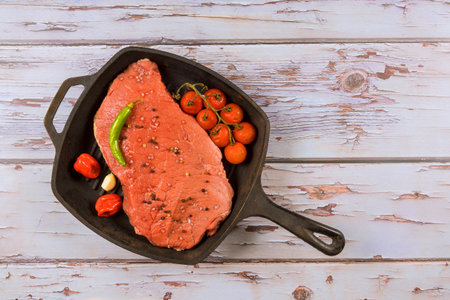 Hearty steak with green pepper and tomatoes rests in skillet on rustic wooden surface.の写真素材