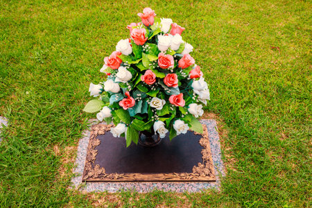 Arrangement of white, pink roses decorates gravestone in peaceful cemetery under farewell ceremony