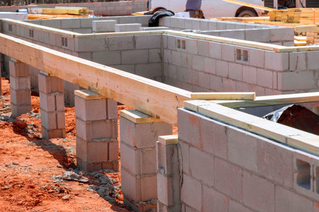Lay down wooden beams on newly constructed foundation of concrete blocks in developing neighborhood.
