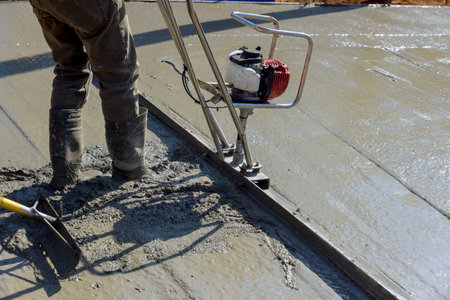 Construction worker uses power trowel to create smooth concrete surface on works day.