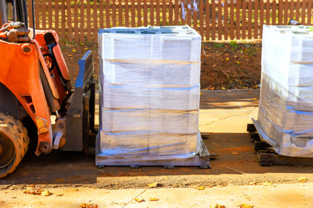 Forklift transporting wrapped cement block pallets in construction site under works day