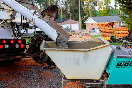 Construction workers wet fresh concrete into wheeled concrete wheelbarrow for pouring fresh concrete mixの写真素材