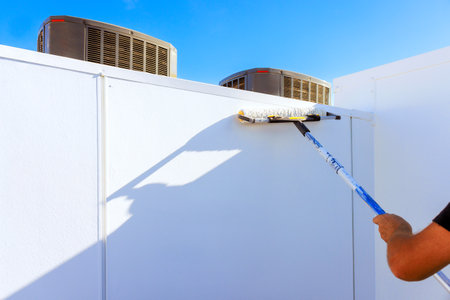 Painter uses roller to paint white wall on rooftop while air conditioning units standの写真素材
