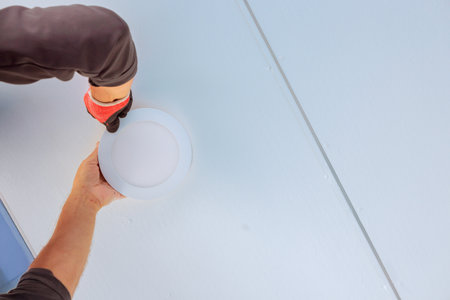 Worker wearing gloves is placing round light fixture onto ceilingの写真素材