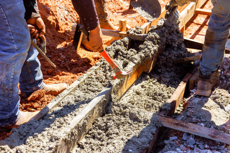 Workers mix pour fresh concrete into wooden forms, preparing foundation under curbed is concrete