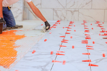 Worker applies adhesive arranges tiles with clips for precise spacing clean finish.の写真素材