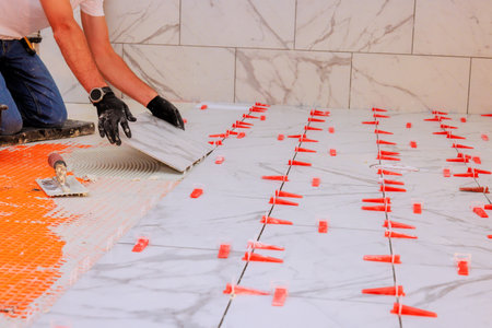 Tiler man is carefully setting white marble tiles on bathroom floor while renovatingの写真素材