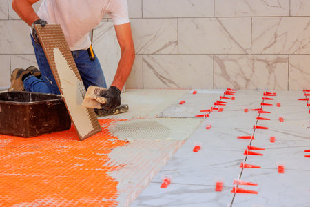 Worker carefully lays ceramic tiles on freshly prepared floor during home improvementの写真素材