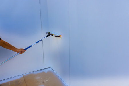 Handyman is using paint roller on wall in bright room, focusing on even coverage.の写真素材
