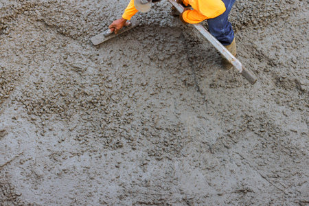 Construction worker skillfully levels wet concrete on surface under foundation works