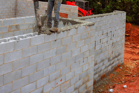Construction worker pours cement on wall being built, surrounded by dirt machinery in work daytimeの写真素材