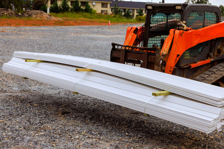 Construction vehicle lifts long white sheets of material at job set