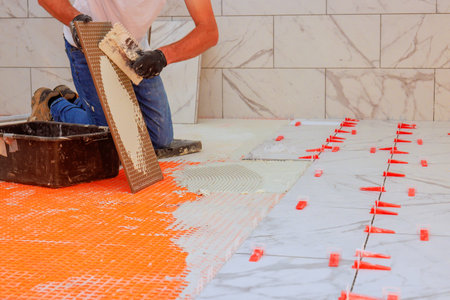 Worker installs marble tiles on bathroom floor using mortar spacers for alignment.の写真素材