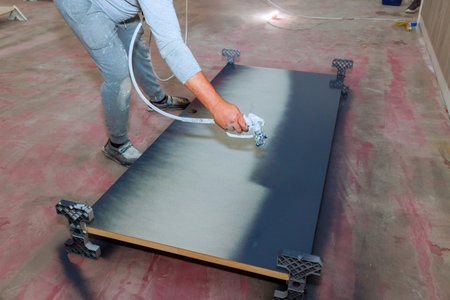 Painter is using spray gun to paint large wooden board in well lit indoor area.