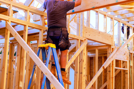Construction worker is on ladder, installing wooden beams in house roofing frameの写真素材