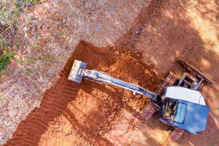Heavy machinery is leveling ground at construction site surrounded by trees autumn.