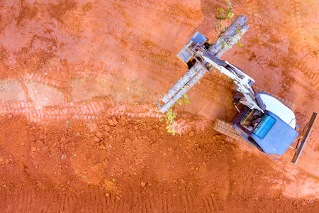 Heavy machinery operates on red soil, remove fallen tree log preparing land for constructionの写真素材