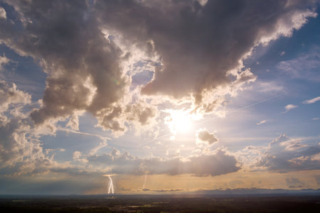 Thunderstorm unfolds with striking lightning, casting stunning glow over landscape as sun sets.