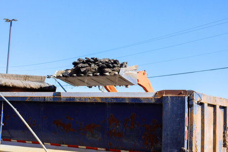 Heavy machinery dumps asphalt debris into truck during road construction project