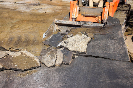 Workers use loader to remove broken asphalt prepare road surface for repairs during demolition...