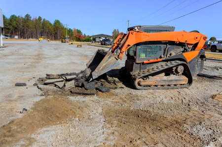 Construction crew is working on commercial site, using skid steer loader to remove asphalt debris