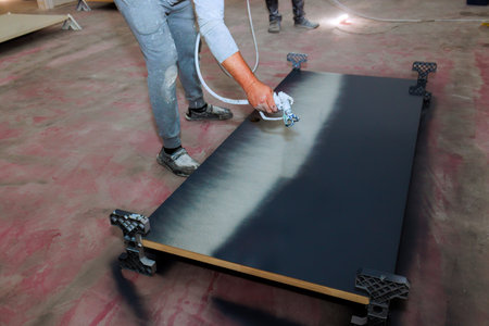 Paint worker uses spray gun to paint large wooden door with black paintの写真素材