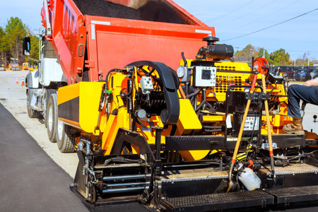 Paving machine lays asphalt as truck unloads hot asphalt for road maintenance roadway works