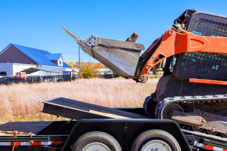 An excavator is unloading materials from flatbed trailer at construction siteの写真素材