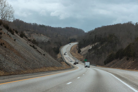 Vehicles travel along American winding highway surrounded by hills overcast skiesの写真素材