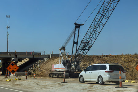 Heavy machinery is actively use crane to lift materials an overpass on highway, affecting traffic...