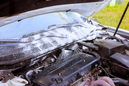 Mechanic uses foam to clean engine compartment of car under hood