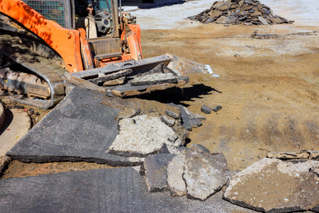 Heavy machinery is breaking up old pavement at construction site while workers prepare for repairs...