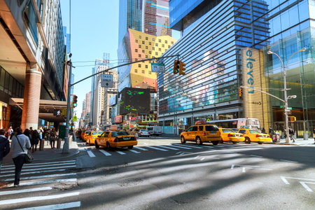 People wait on sidewalk while yellow taxis drive through busy New York City street on Manhattan