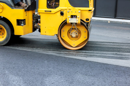 Heavy roller asphalt compactor compacts new asphalt on city street under smooth surface.